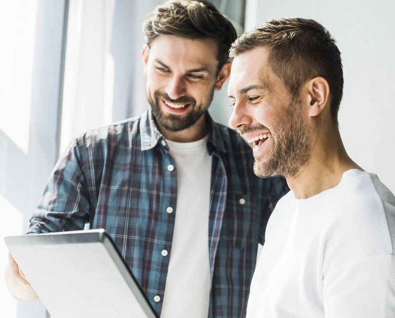 Dos profesionales sonrientes revisando una laptop en un entorno de oficina.