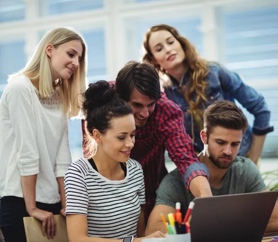 Cinco profesionales colaborando juntos con una notebook en un espacio de trabajo