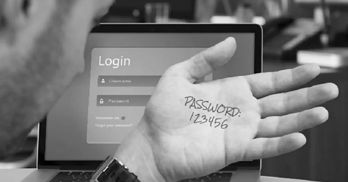 Persona leyendo una contraseña simple en su mano, con una pantalla con formulario de inicio de sesiòn detràs