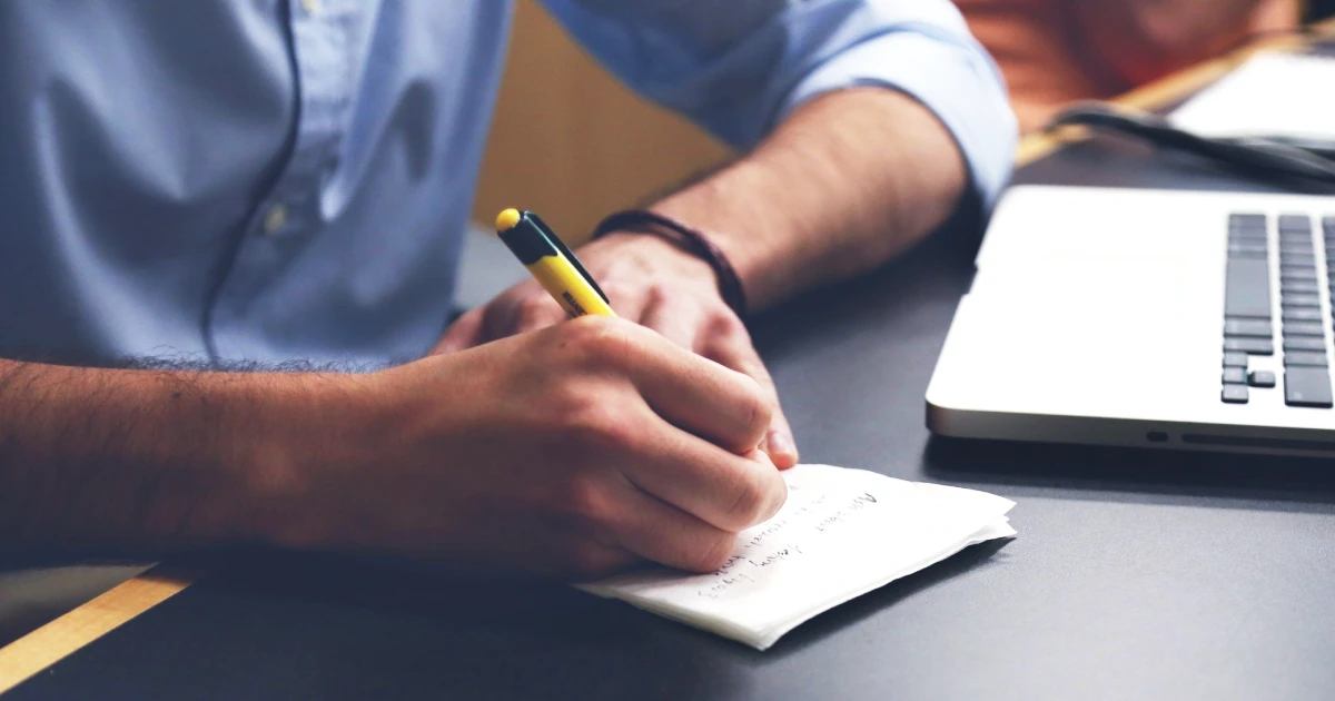 Persona escribiendo tareas a mano frente a una notebook, como parte del proceso de identificar tareas repetitivas para automatizar